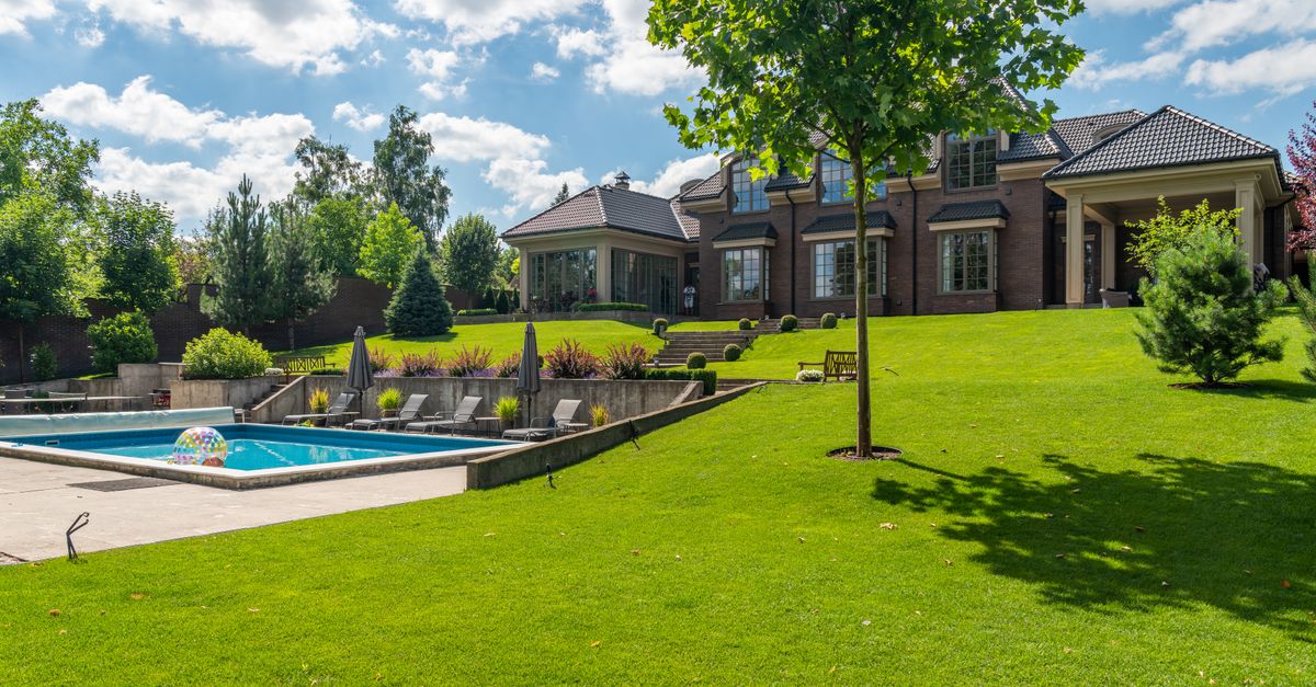 Spacious elegant mansion with a pristine pool, lush garden, and clear blue sky.